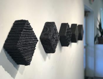 Four black sculptures hanging on a wall.