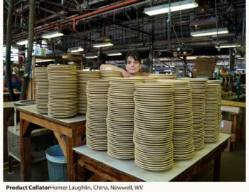 A woman peeks over large stacks of ceramic plates in an industrial setting at the Homer Laughlin China Company in Newell, West Virginia.