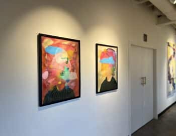 Framed abstract paintings on a white wall in a hallway, featuring colorful cloud-like shapes.